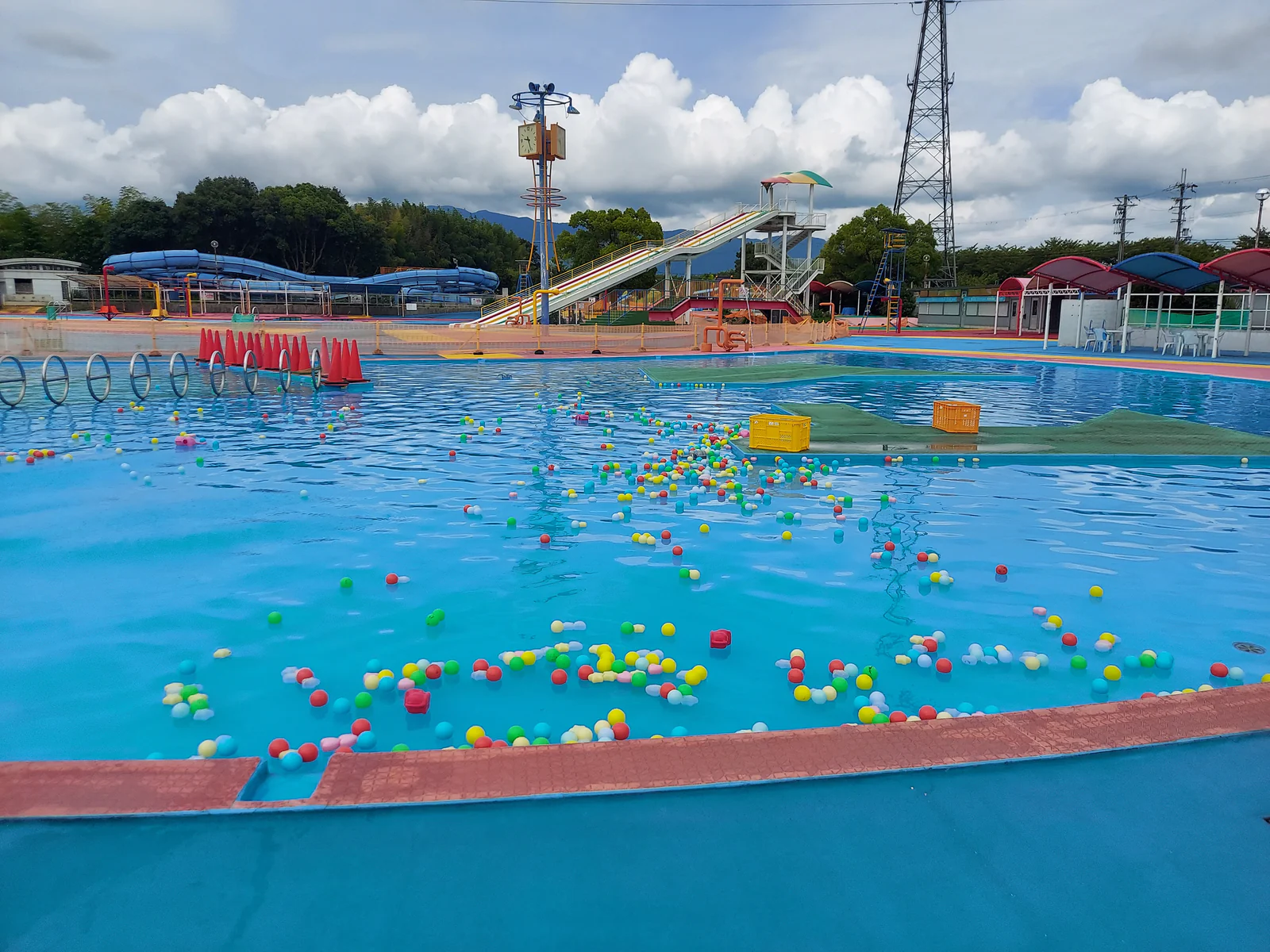 橿原じゃぶじゃぶパークの水遊びエリア。浅いプールにカラフルなボールやマットが浮かび、奥にスライダーが見える